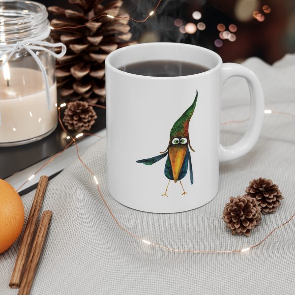 White ceramic coffee mug with a watercolor painting of a whimsical crow called Bubba mug is on a table with chesnuts