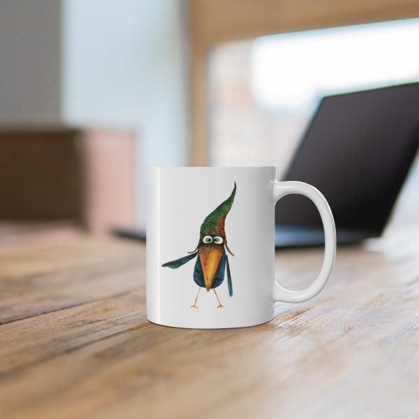 White ceramic coffee mug with a watercolor painting of a whimsical crow called Bubba mug is on a table
