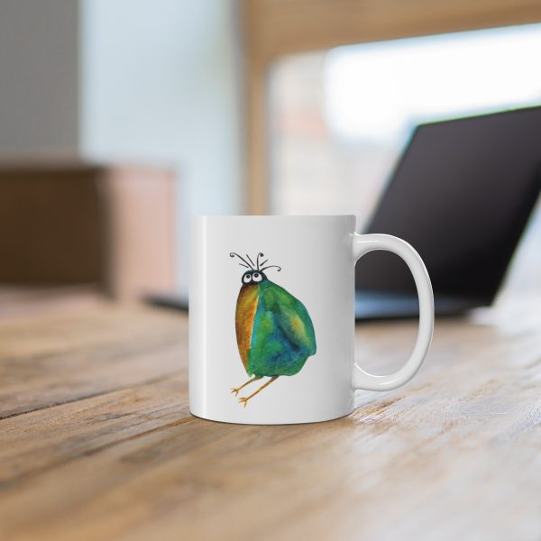 White ceramic coffee mug with a watercolor painting of a whimsical crow called Screech the mug is on a table