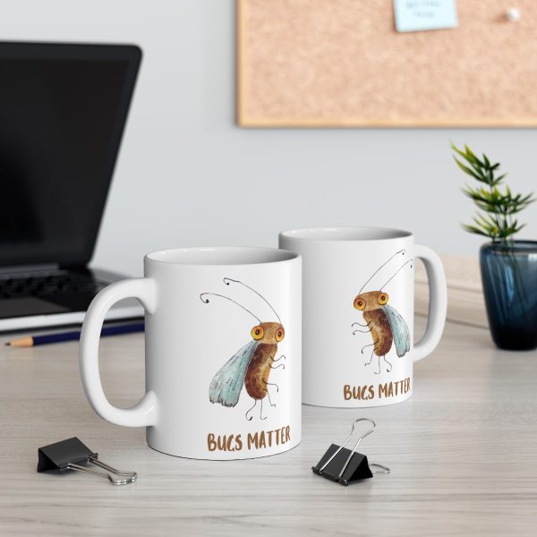 two white ceramic coffee mugs with a watercolor painting of a startled fruit fly the mugs are on a table