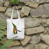 a white canvas tote bag featuring a watercolor painting of a whimsical crow bag is hanging on a wall