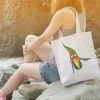 girl on rocky beach with a white canvas tote bag featuring a watercolor painting of a whimsical crow