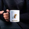 Woman in black blouse holding a white coffee mug with a whimsical watercolor illustration of a fruit fly