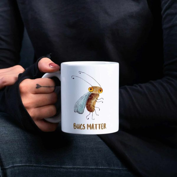 Woman in black blouse holding a white coffee mug with a whimsical watercolor illustration of a fruit fly