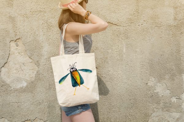 woman with a white canvas tote bag featuring a watercolor painting of a whimsical crow