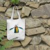 a white canvas tote bag featuring a watercolor painting of a whimsical crow bag is hanging on a wall