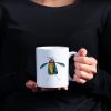 Woman in black blouse holding a white ceramic 11 oz coffee mug with a whimsical watercolor illustration of a crow