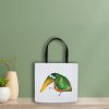 white polyester tote bag featuring a watercolor illustration of a whimsical crow the bag is leaning against a sage green wall