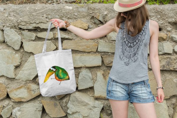 Girl holding a white canvas tote bag featuring a watercolor painting of a whimsical crow