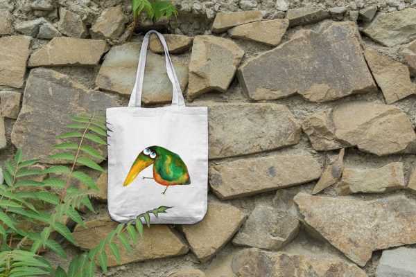 a white canvas tote bag featuring a watercolor painting of a whimsical crow hanging on a wall