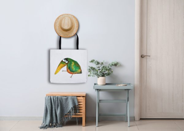 white polyester tote bag featuring a watercolor illustration of a whimsical crow the bag is hanging in a hall