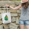 girl holding a white canvas tote bag featuring a watercolor painting of a whimsical crow
