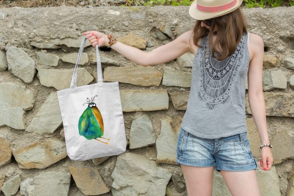 girl holding a white canvas tote bag featuring a watercolor painting of a whimsical crow
