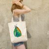 girl with a white canvas tote bag featuring a watercolor painting of a whimsical crow