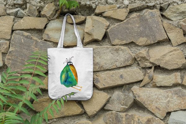 a white canvas tote bag featuring a watercolor painting of a whimsical crow bag is hanging on a wall
