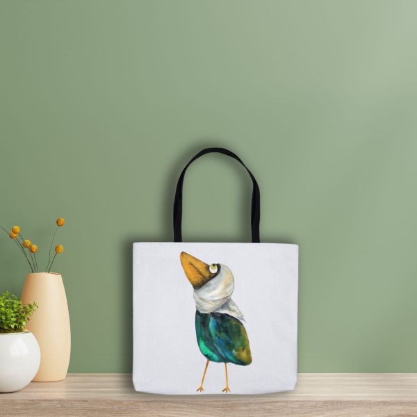 White Tote Bag leaning on a green wall the bag is featuring a watercolor painting of a whimsical crow called Squawk