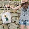girl holding a white canvas tote bag featuring a watercolor painting of a whimsical crow