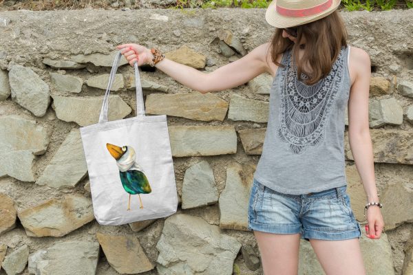 girl holding a white canvas tote bag featuring a watercolor painting of a whimsical crow