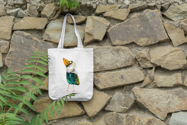 a white canvas tote bag featuring a watercolor painting of a whimsical crow bag is hanging on a wall