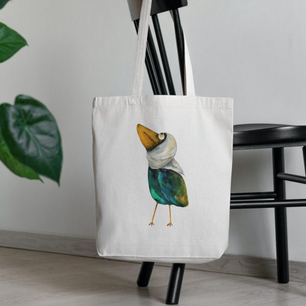 a white canvas tote bag featuring a watercolor painting of a whimsical crow bag is on a chair