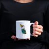 woman in black blouse holding a White ceramic coffee mug with a watercolor painting of a whimsical crow called Squawk