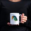 Woman in black blouse holding a white ceramic 11 oz coffee mug with a whimsical watercolor illustration of a cros