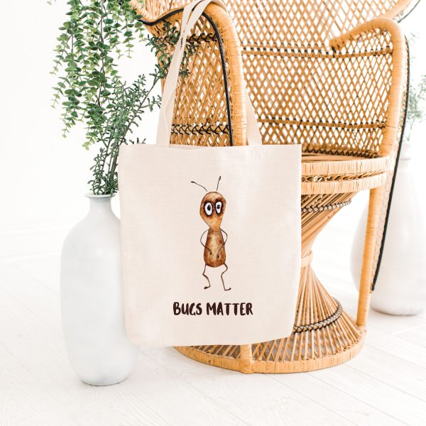 white canvas tote bag with a watercolor painting of a whimsical ant bag is on a bamboo chair