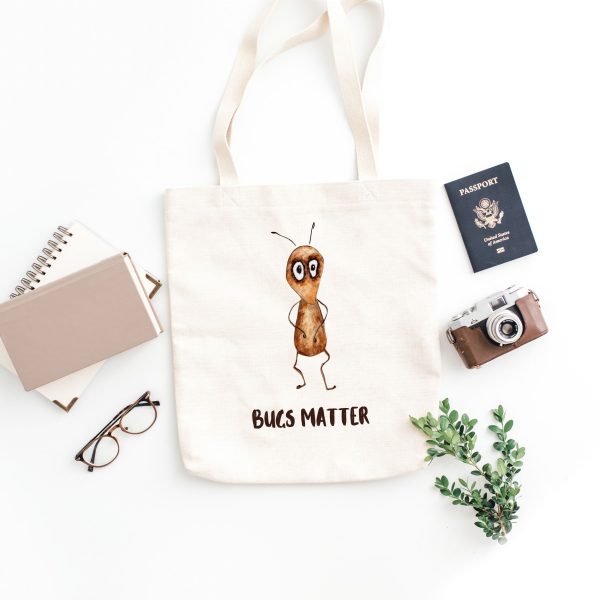 white canvas tote bag with a watercolor painting of a whimsical ant bag is on the floor