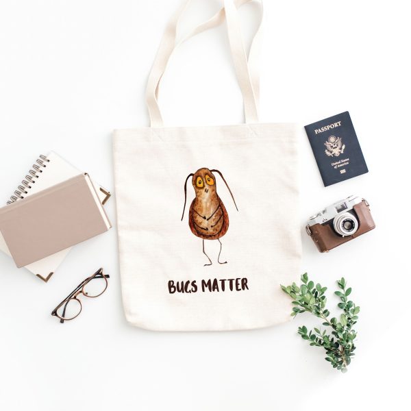 white canvas tote bag with a watercolor painting of a whimsical cockroach bag is on the floor