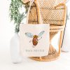 white canvas tote bag with a watercolor painting of a whimsical mosquito bag is hanging on a bamboo chair