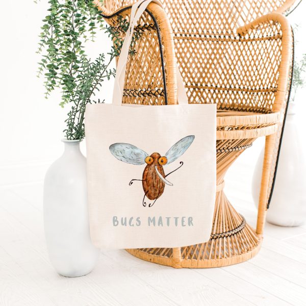 white canvas tote bag with a watercolor painting of a whimsical mosquito bag is hanging on a bamboo chair