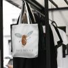white canvas tote bag with a watercolor painting of a whimsical mosquito bag is hanging on a rack