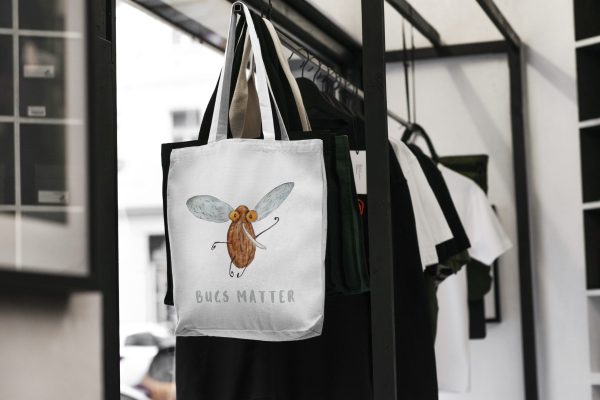 white canvas tote bag with a watercolor painting of a whimsical mosquito bag is hanging on a rack