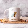 White ceramic coffee mug with a watercolor painting of a whimsical fruit fly the mug is on a table with leaves