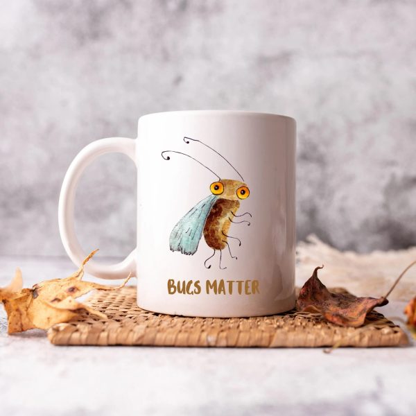 White ceramic coffee mug with a watercolor painting of a whimsical fruit fly the mug is on a table with leaves
