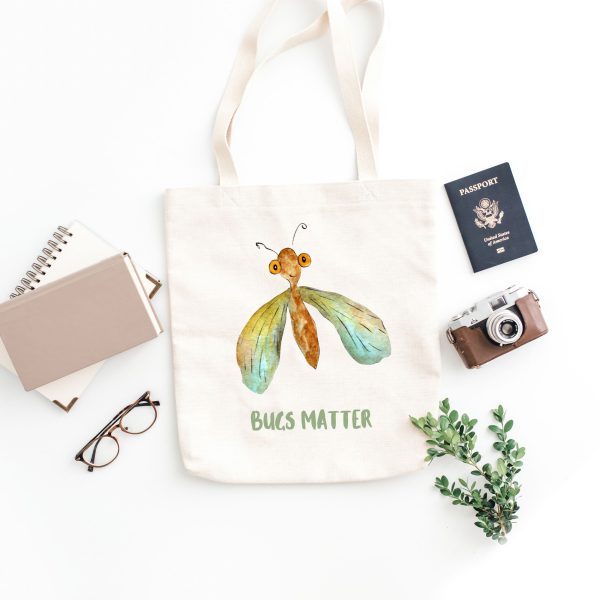 white canvas tote bag with a watercolor painting of a whimsical green lacewing bag is on the floor