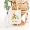 white canvas tote bag with a watercolor painting of a whimsical green lacewing bag is hanging on a chair