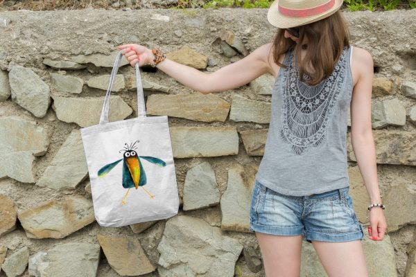 woman holding a white canvas tote bag featuring a watercolor painting of a whimsical crow